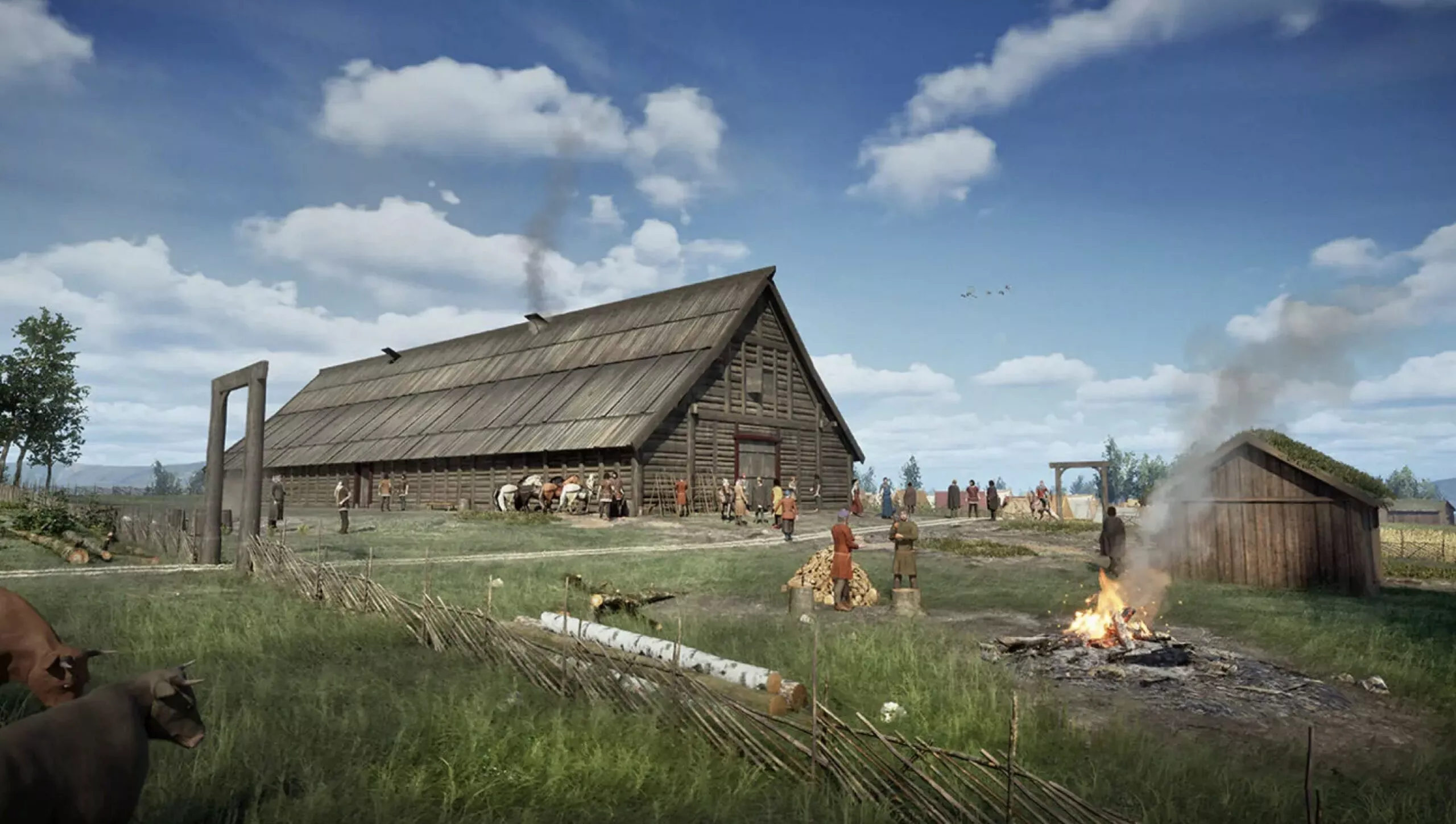 Et rekonstrueret landsbybillede fra vikingetiden med et stort langhus af træ, folk samlet udenfor, køer, der græsser, og røg, der stiger op fra et bål - ved bygningen stammede fra vikingetiden. En klar blå himmel med spredte skyer fuldender udsigten.