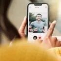En person, der holder en smartphone og bruger en dating-app, ser en profil af en smilende mand i en grå skjorte ved navn Daniel, 27 år, med mulighed for at synes godt om eller ikke synes godt om profilen.