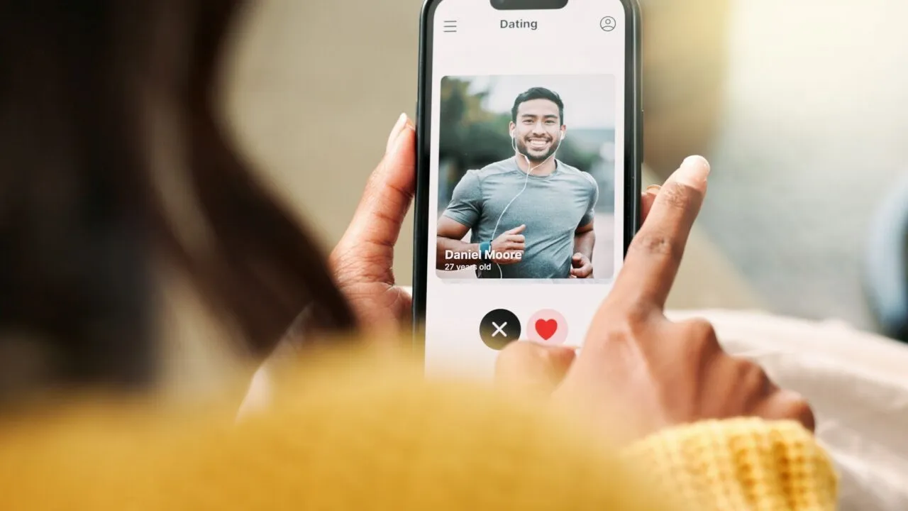 En person, der holder en smartphone og bruger en dating-app, ser en profil af en smilende mand i en grå skjorte ved navn Daniel, 27 år, med mulighed for at synes godt om eller ikke synes godt om profilen.