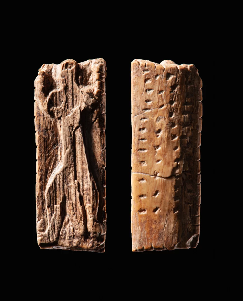 To billeder af et rektangulært gammelt udskåret objekt; på den ene side ses en menneskefigur i relief, mens den anden side viser rækker af små indridsede mærker, alt sammen på en sort baggrund.