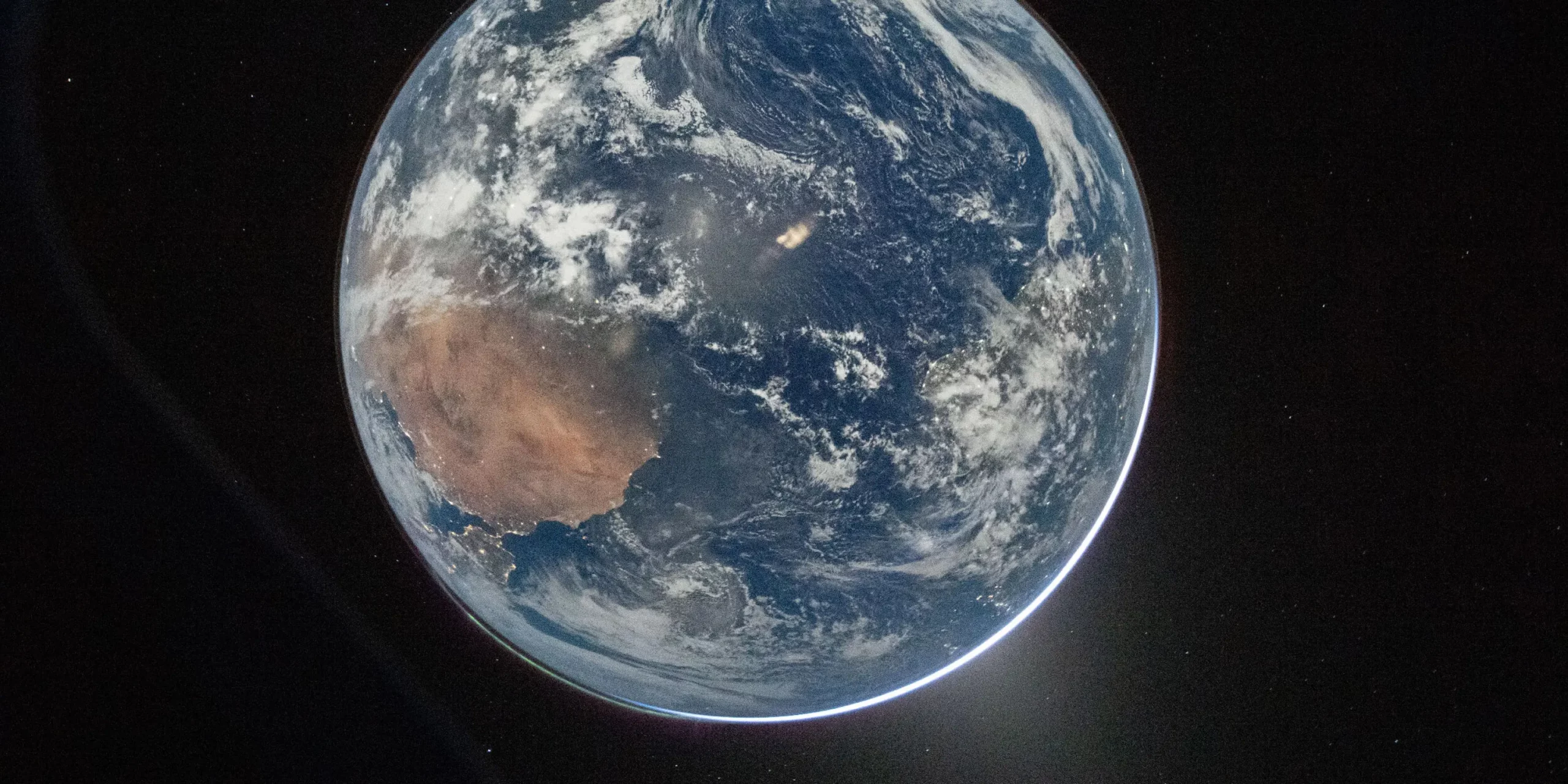 Et billede af Jorden fra rummet viser skyer, blå oceaner og det brune landskab på et kontinent, hvor sollyset oplyser planetens kant mod rummets mørke.