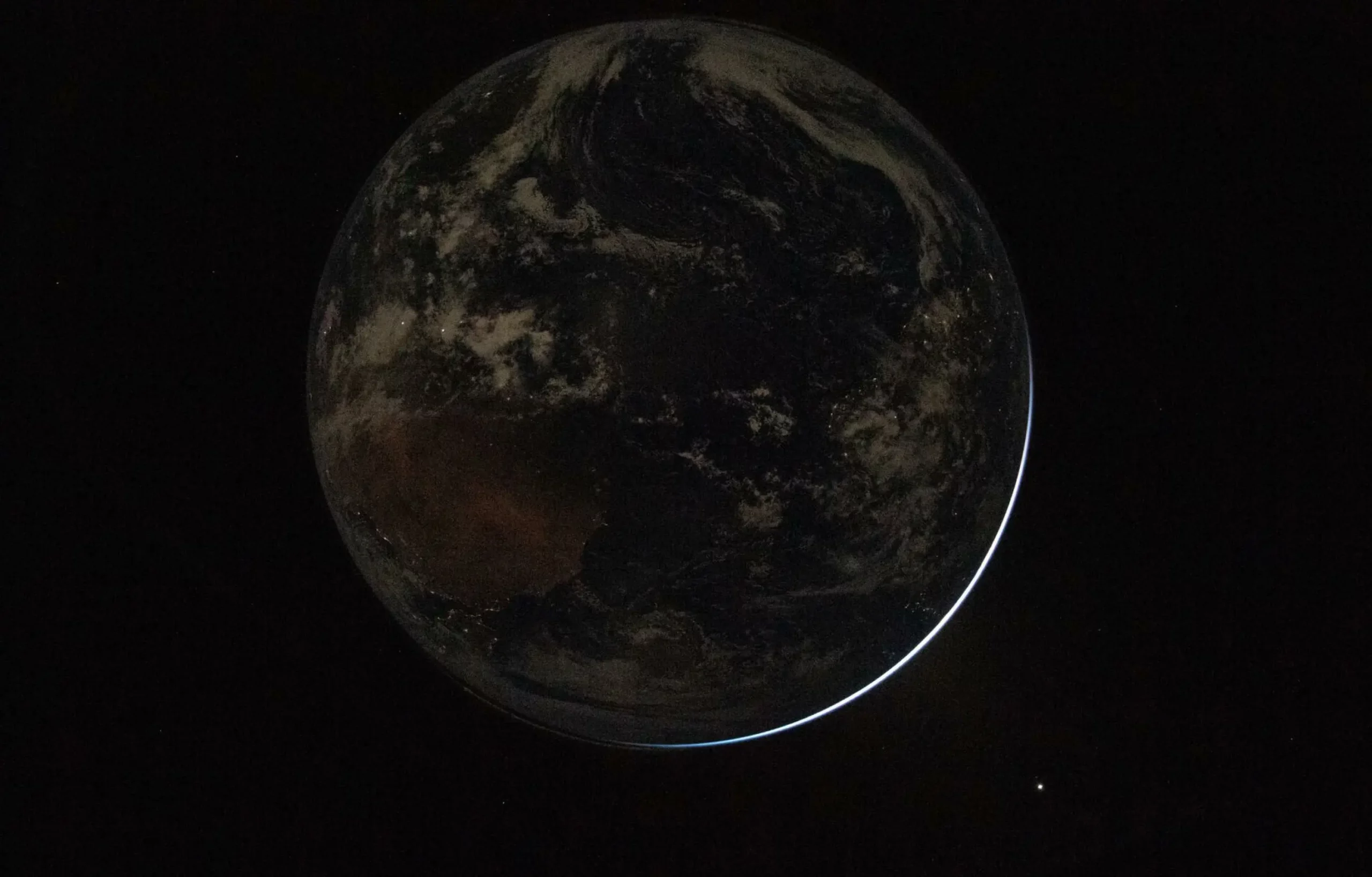 Et delvist skygget billede af Jorden fra rummet med en tynd halvmåne af sollys langs kanten og et fjernt lyspunkt mod den mørke baggrund.