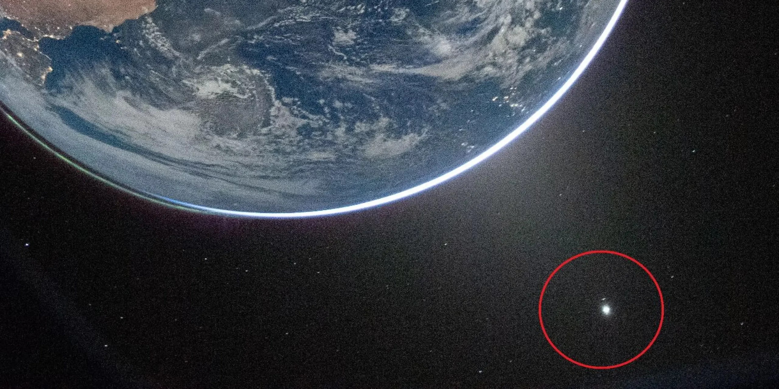 Udsigt til Jorden fra rummet med en del af planeten synlig øverst til venstre og en lysende prik fremhævet af en rød cirkel i rummets mørke nederst til højre.