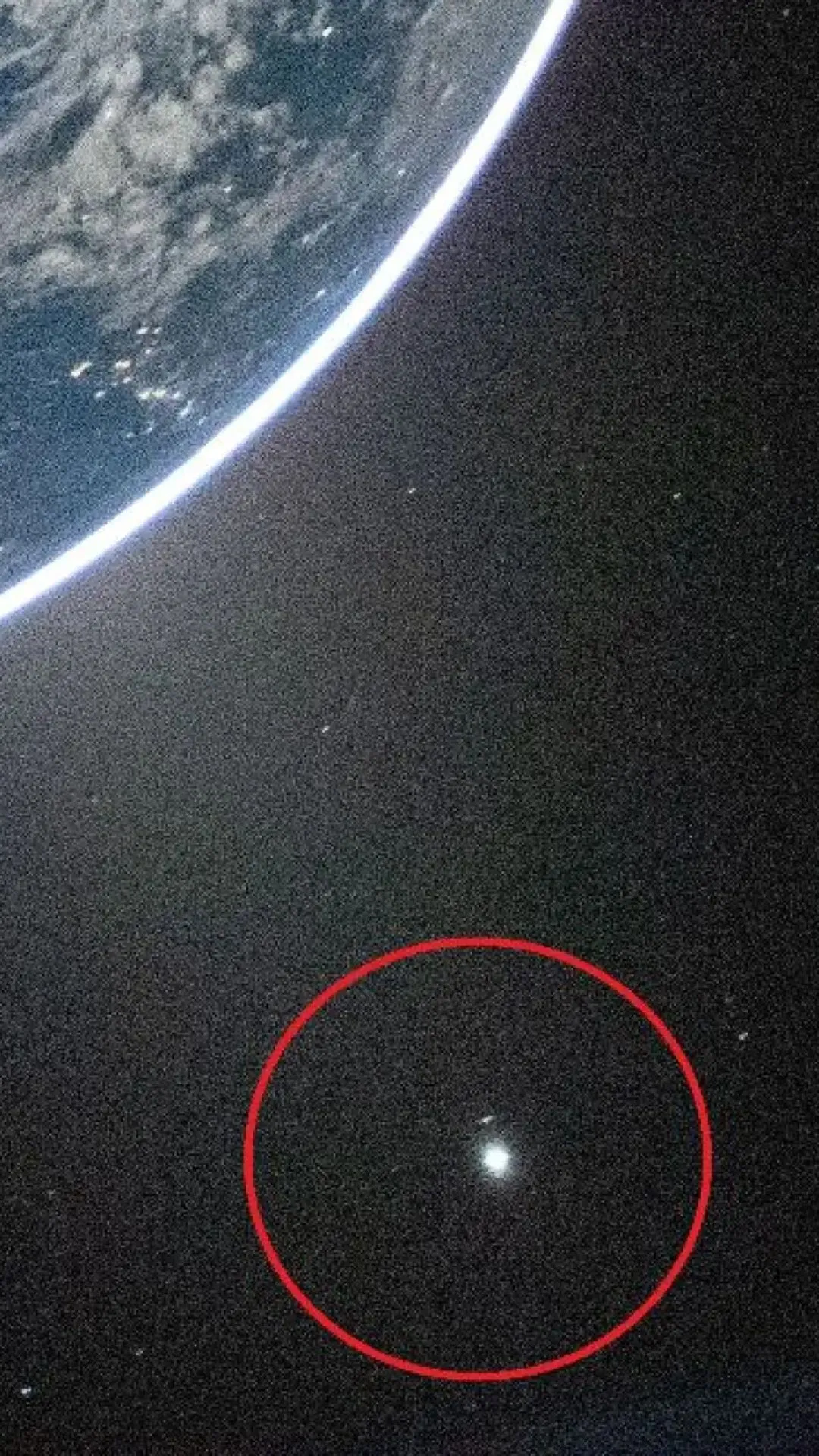 Udsigt til Jorden fra rummet med en del af planeten synlig øverst til venstre og en lysende prik fremhævet af en rød cirkel i rummets mørke nederst til højre.