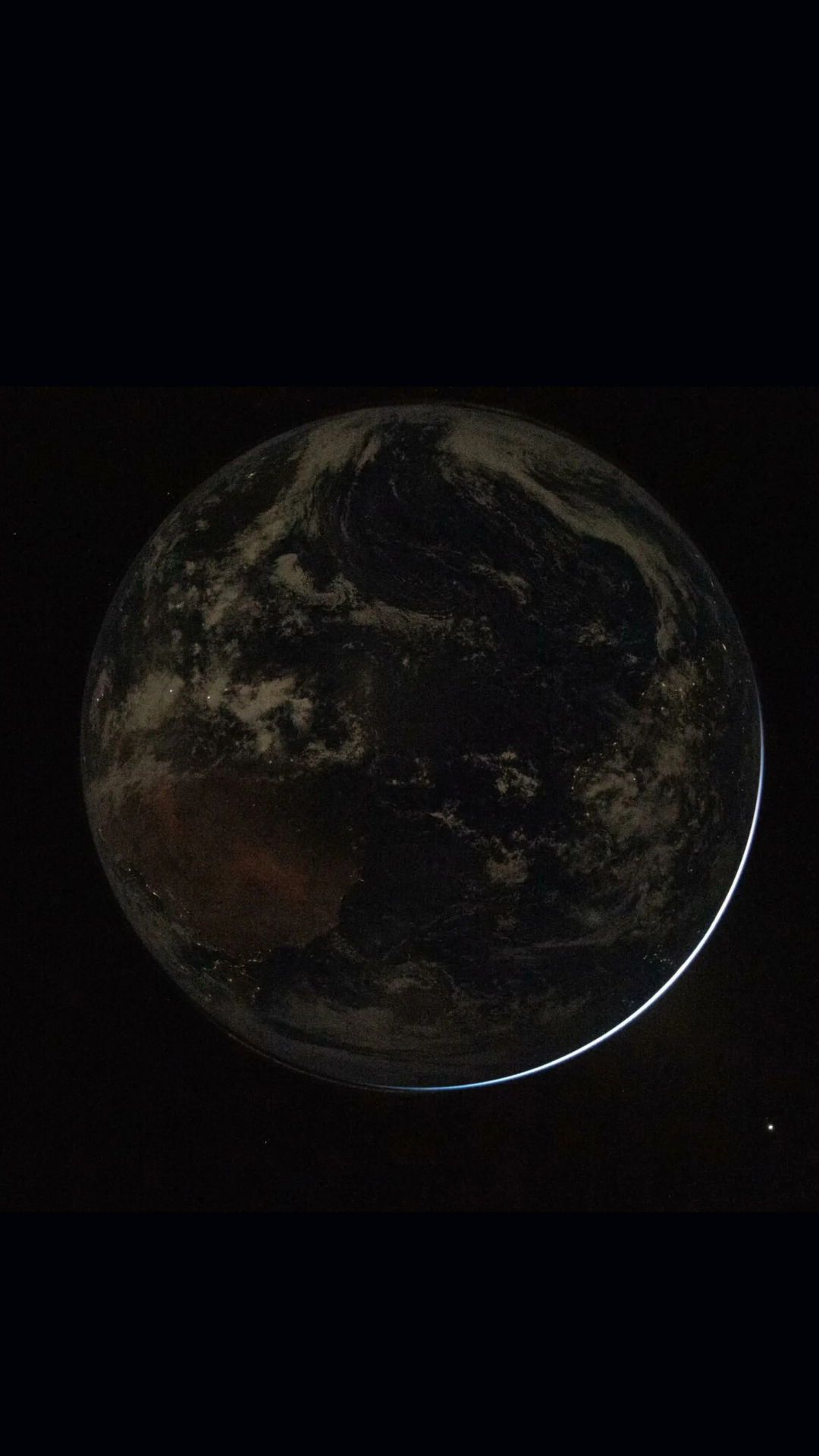 Et mørkt, delvist skyggelagt billede af Jorden fra rummet, der viser skymønstre og kontinenter, med det meste af planeten i svagt lys mod en sort baggrund.