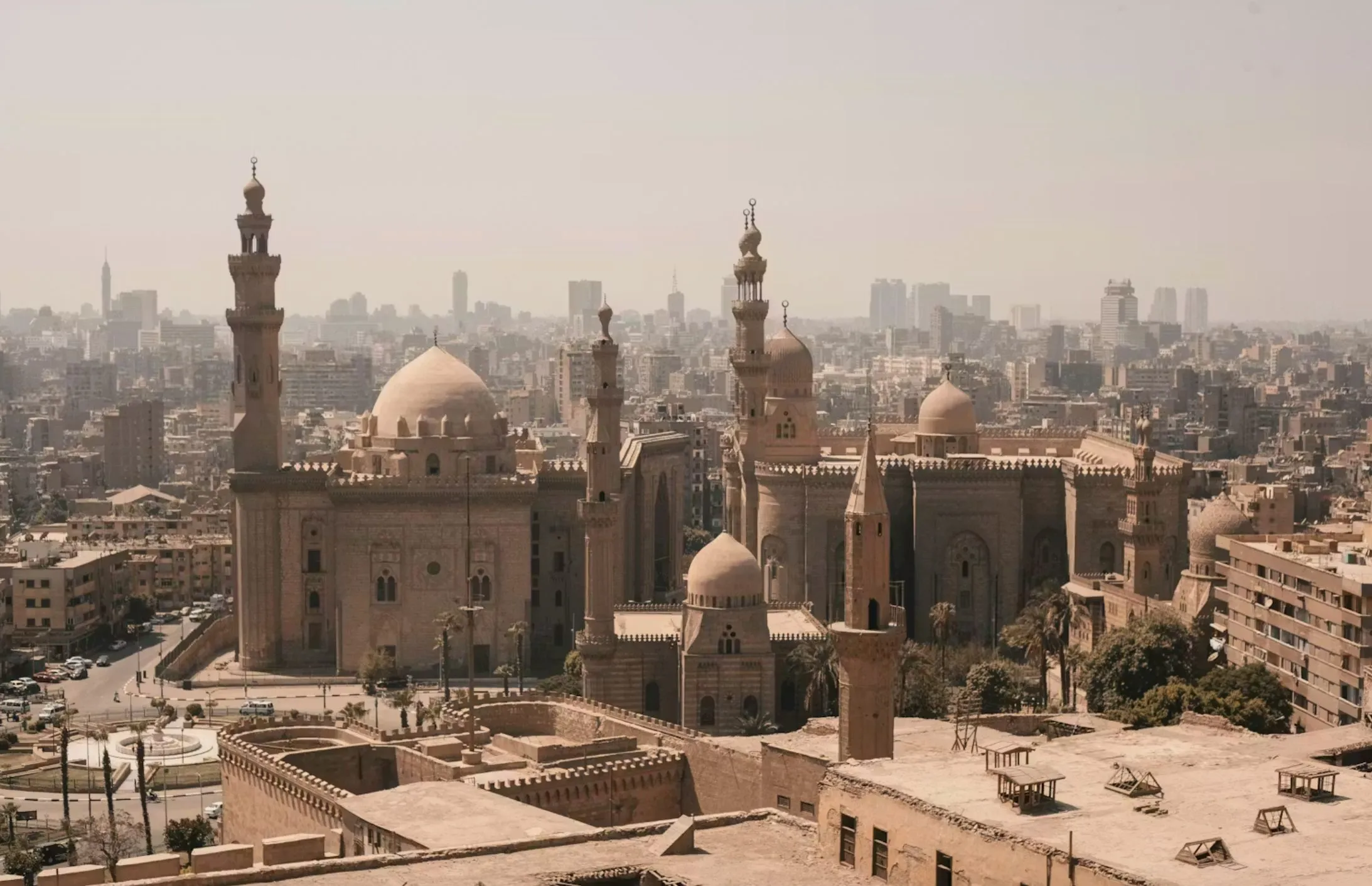 Et diset bybillede med store historiske moskéer med kupler og minareter i forgrunden mod en vidtstrakt byskyline under en lys himmel.