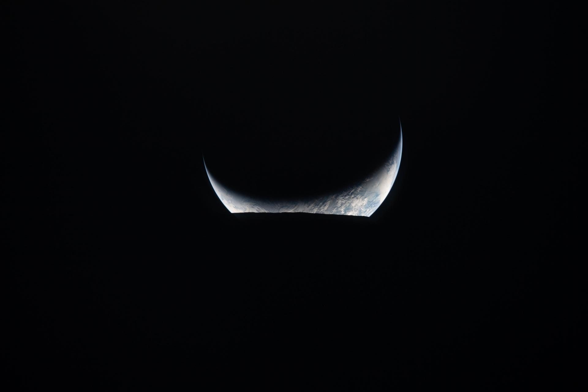 En tynd halvmåne af Jorden er oplyst mod det sorte rum, hvor det meste af planeten ligger i skygge, og kun en lille del viser blå og hvide farver.