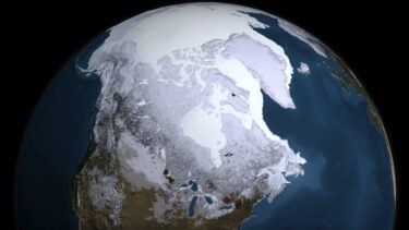 Et billede af Jorden fra rummet, der viser den arktiske region dækket af hvid is og sne med dele af Nordamerika, Grønland og Det Arktiske Ocean synlige. Det omgivende hav er dybblåt.
