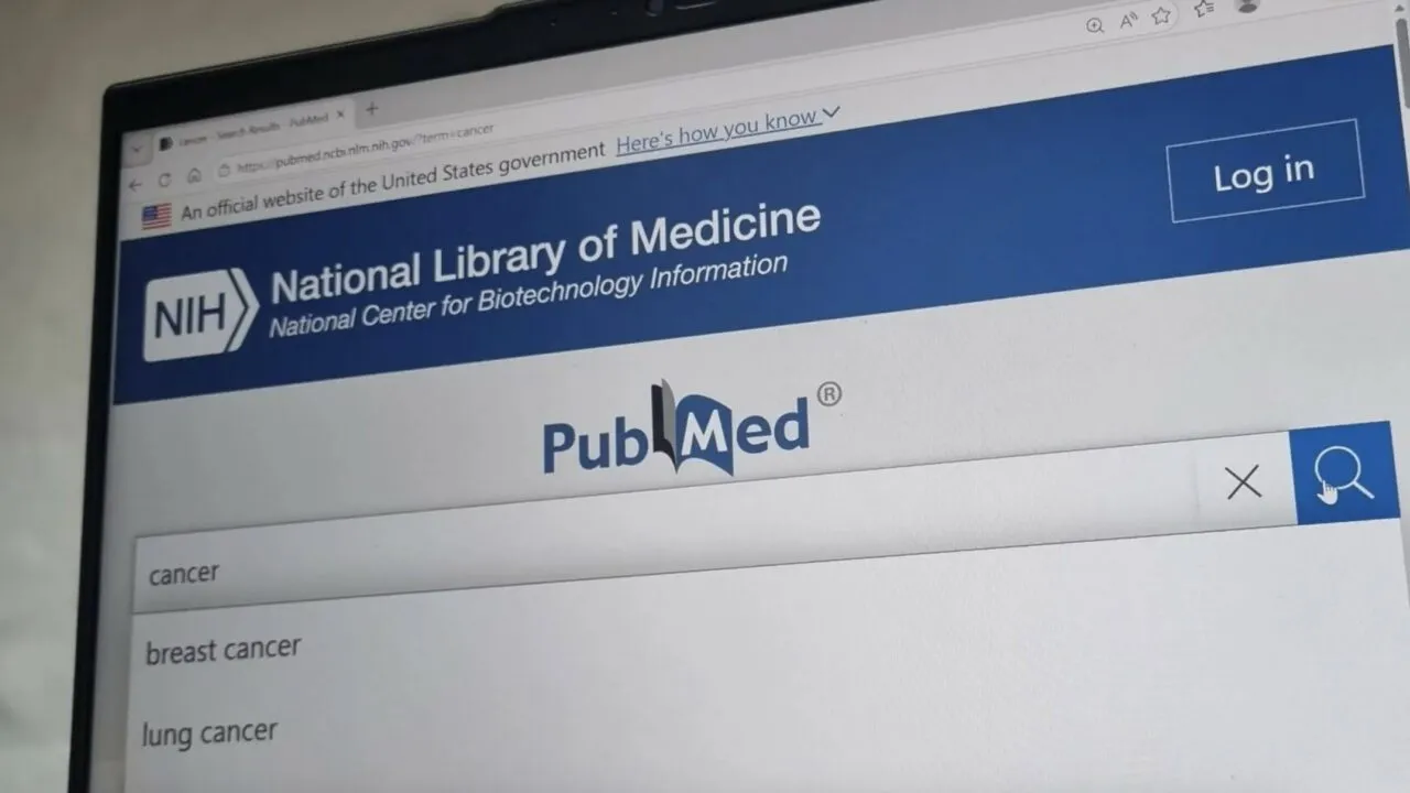 En computerskærm viser PubMed-webstedet fra National Library of Medicine og viser en søgning på "cancer" med forslag til "breast cancer" og "lung cancer". En blå "Log ind"-knap vises i øverste højre hjørne.