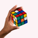 En hånd holder en blandet Rubiks terning foran en ensfarvet, lys baggrund.