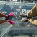Turister poserer på et glasgulv i en skyskraber.
