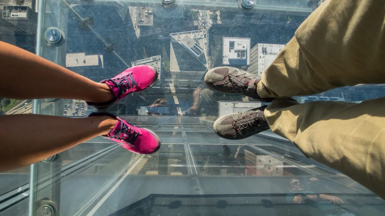 Turister poserer på et glasgulv i en skyskraber.