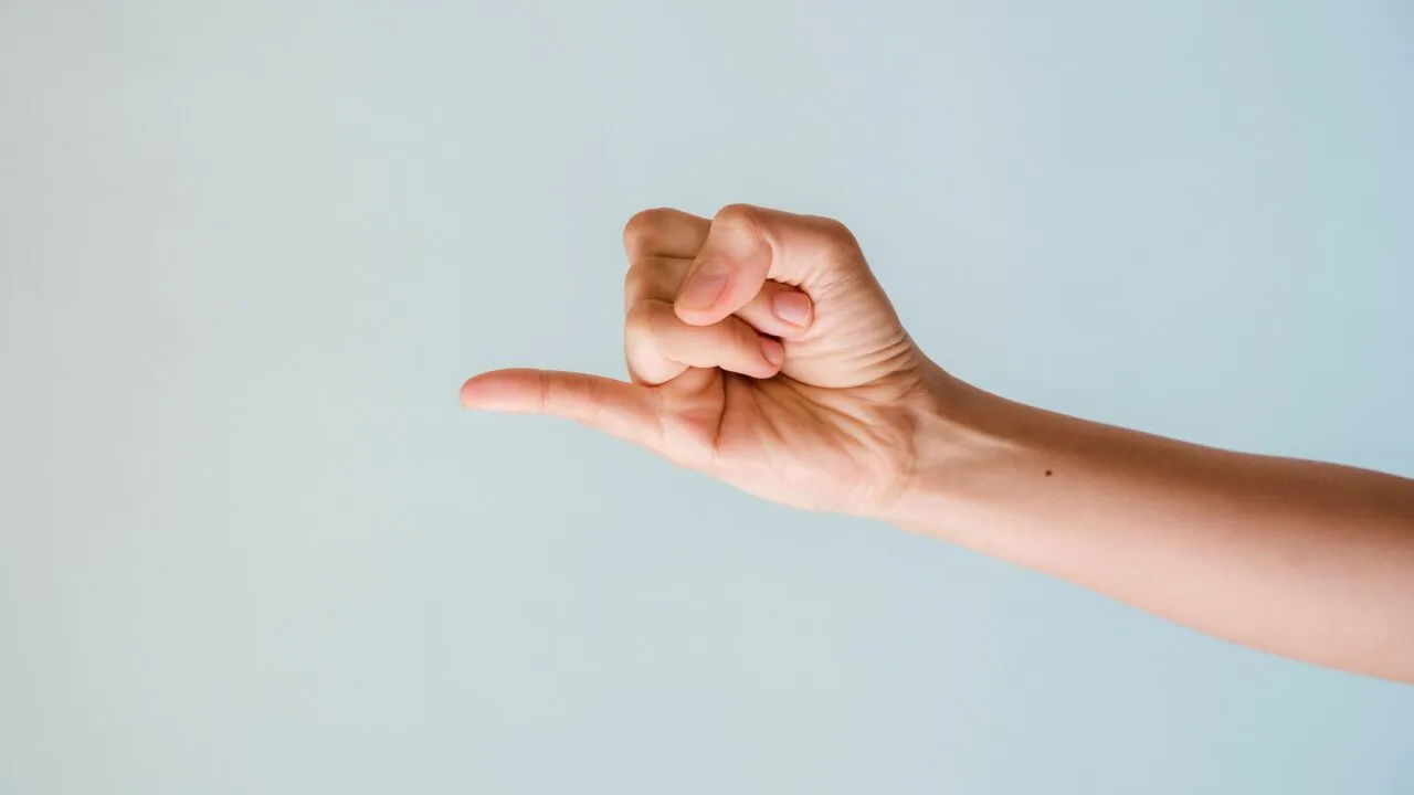 En hånd, der strækkes fremad mod en lyseblå baggrund, med lillefingeren løftet og de øvrige fingre krummet ind mod håndfladen, hvilket danner »pinky promise«-gesten.