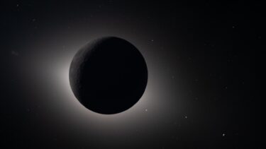 En mørk, skyggefuld planet eller måne er omgivet af en lysende glorie i rummet, som en solformørkelse set fra rummet, med mange svage stjerner spredt ud i baggrunden.