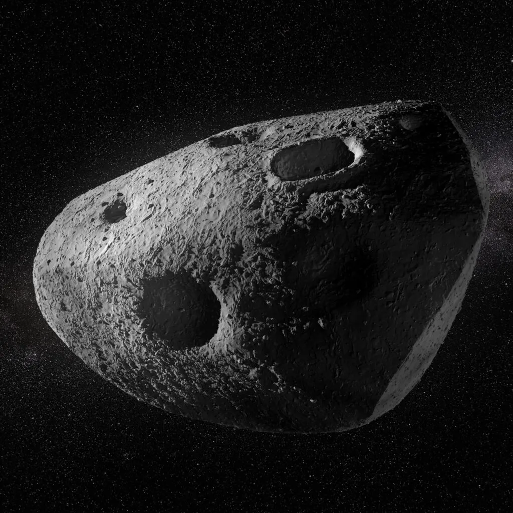 En grå, klippefyldt asteroide med adskillige store kratere svæver i det mørke rum. I baggrunden ses spredte stjerner og et svagt, tåget bånd, der ligner Mælkevejen.