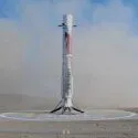 En raketbooster lander lodret på en cirkulær landingsplads i en ørken og hvirvler støv op. Boosteren bærer LandSpace-logoet, og himlen er klar og blå.