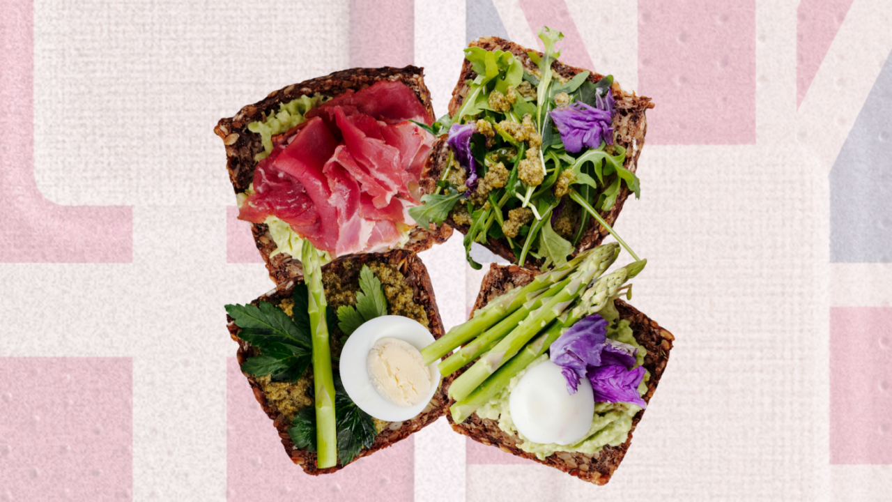 Fire åbne smørrebrød på mørkt brød, belagt med prosciutto, grønne blade, asparges, hårdkogte æg og spiselige blomster, anrettet på en baggrund, der ligner Union Jack-flagget i dæmpede farver.