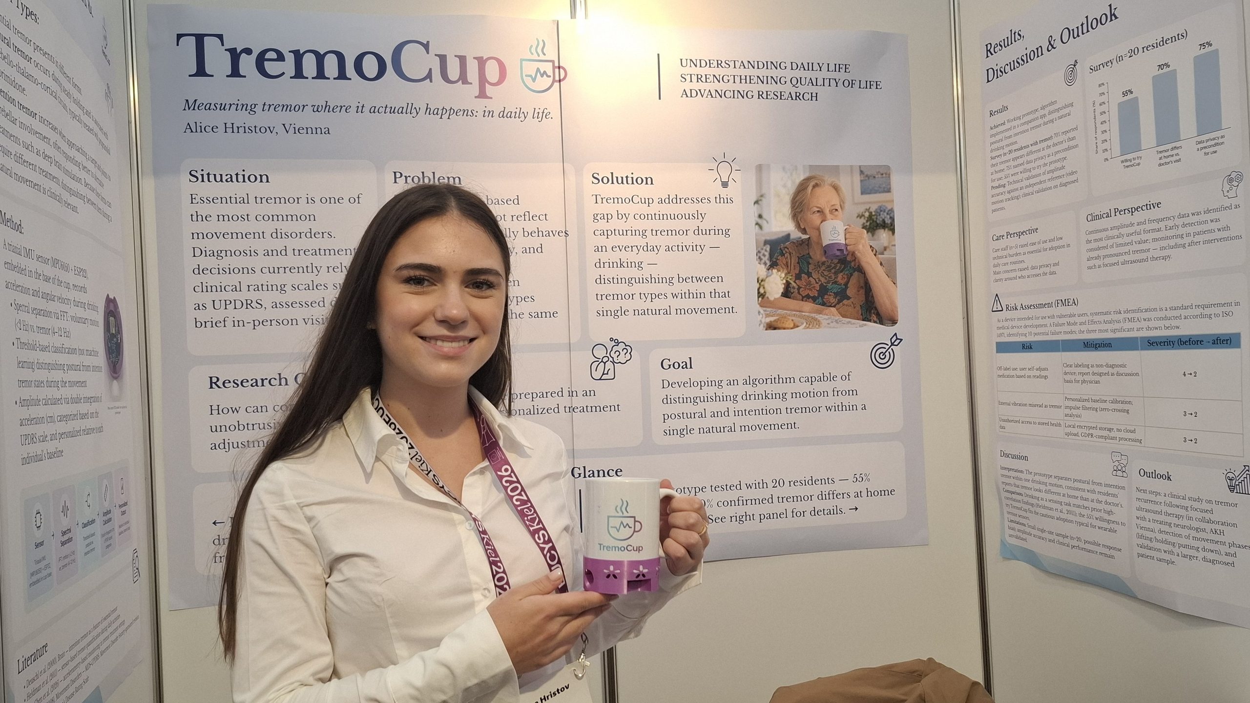 En kvinde står foran en videnskabelig plakat om TremoCup, smiler og holder en kop med TremoCup-logoet. Plakaten beskriver måling af rysten i hverdagen og indeholder diagrammer, tekst og et foto af en kvinde, der drikker.