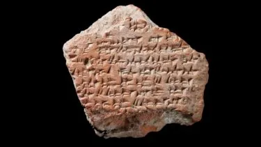 Et fragment af en gammel lertavle med indskrifter i kileskrift, udstillet på en sort baggrund.