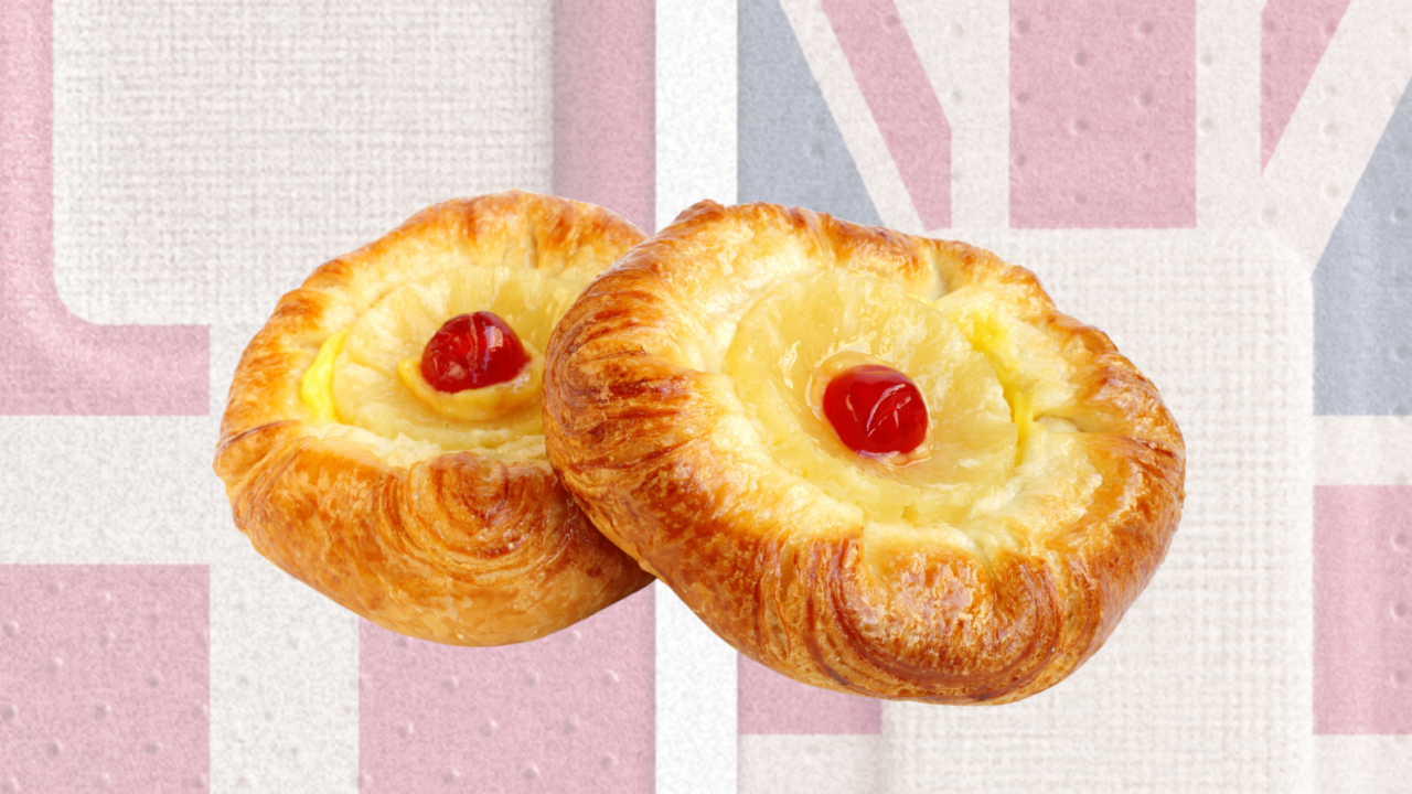 To wienerbrød med cremefyld og røde kirsebær ligger foran en falmet Union Jack-baggrund.