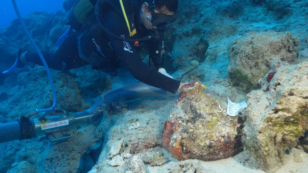 En dykker bruger et sugeslange til at fjerne sediment fra en stengenstand, der ligger neddykket på havbunden.