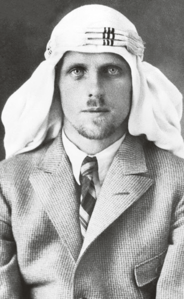 T. E. Lawrence iført en keffiyeh, en skjorte med krave, et stribet slips og en jakke.