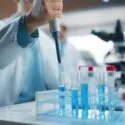 En forsker, der bruger en pipette til at overføre blå væske til et reagensglas i et laboratorium.