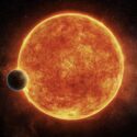 En stor, lys, orange sol med en mindre, klippefyldt planet i forgrunden.