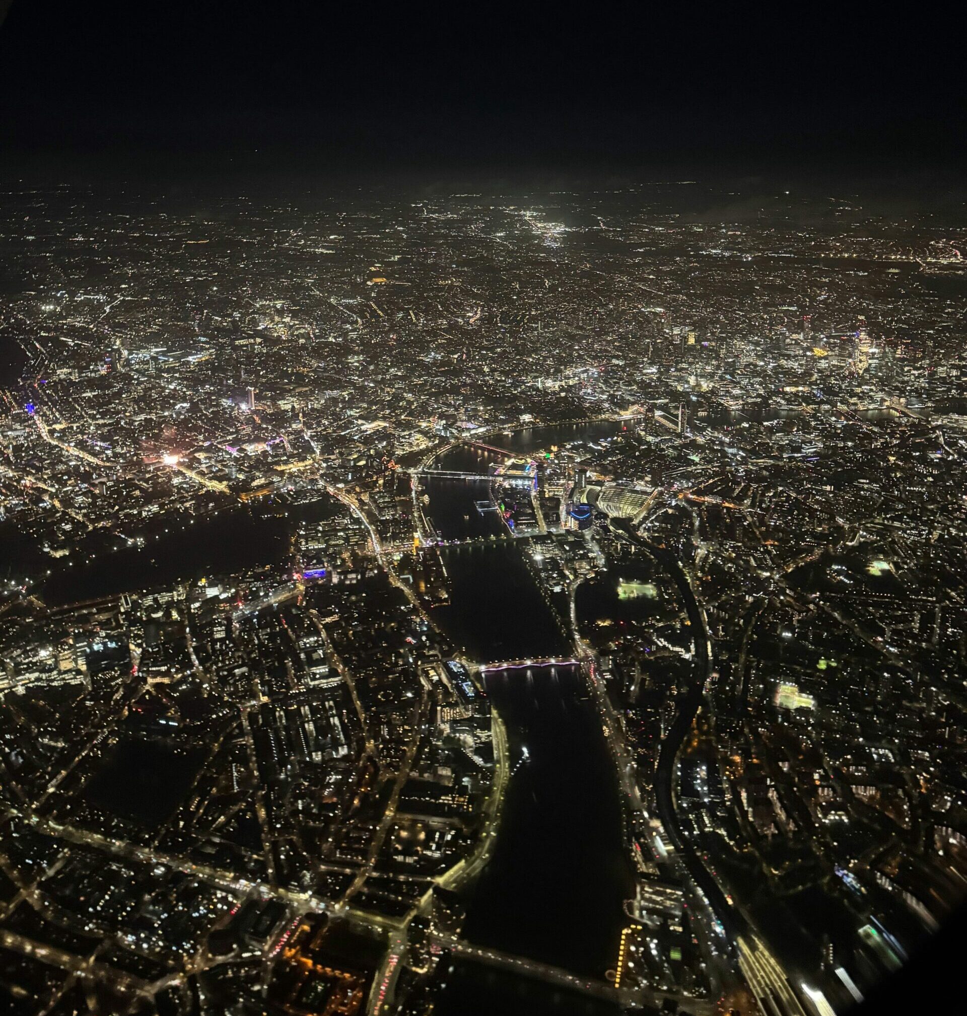 Nattlig luftfoto af London, der viser byens lys og Themsen, der snor sig gennem byens centrum.