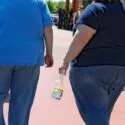 To personer i T-shirts og jeans går ned ad en asfalteret sti; den ene bærer en lille plastikpose, og den anden en sort håndtaske.