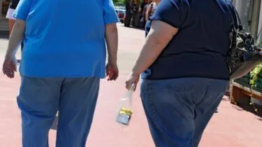 To personer i T-shirts og jeans går ned ad en asfalteret sti; den ene bærer en lille plastikpose, og den anden en sort håndtaske.